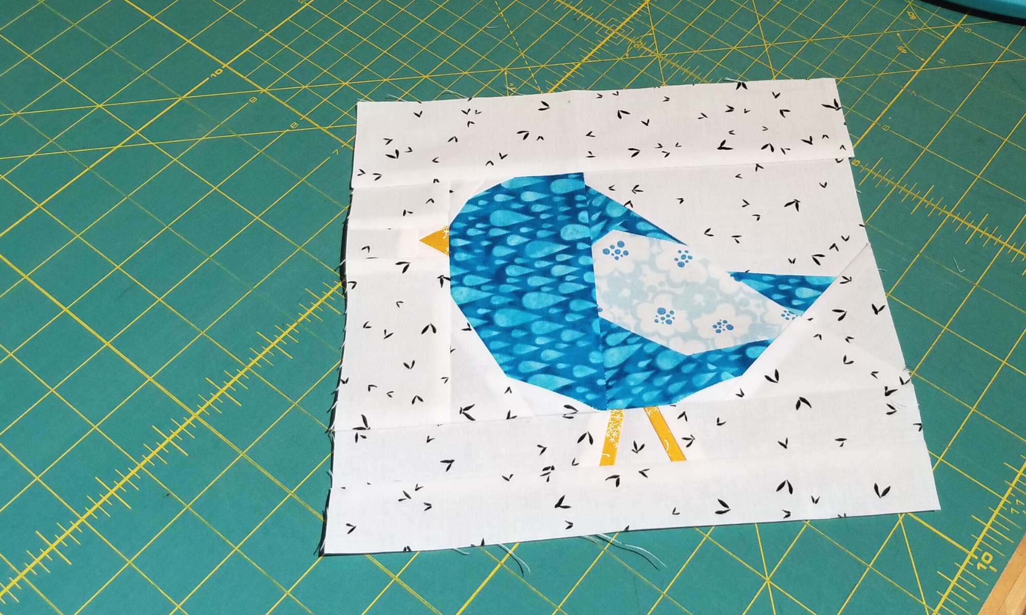 a quilt block featuring a blue bird laying on a cutting mat